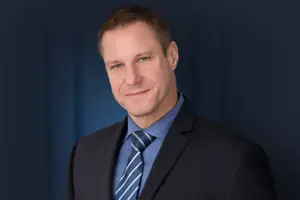 A man in a black suit and tie smiling for a photo