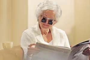 An elderly woman wearing glasses and reading a newspaper