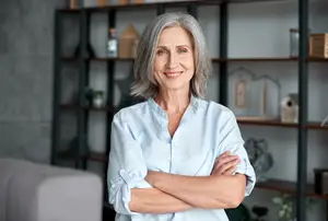 Happy mature woman standing in a living room with her arms crossed