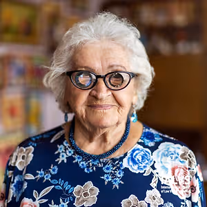 Portrait of an elderly woman with glasses and a floral dress smiling for the camera