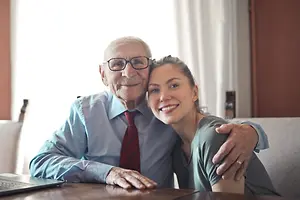 Elderly man and woman sitting on a couch in a living room, smiling for the camera.