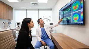 A man and woman are standing in front of a screen. The man is pointing at the screen and the woman is looking at him.