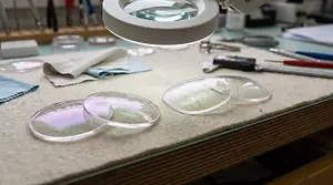 An overhead shot of a magnifying glass, lenses, and other tools on a workbench
