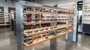 A display of sunglasses in a retail store with multiple shelves of different colors and styles, illuminated by lights.