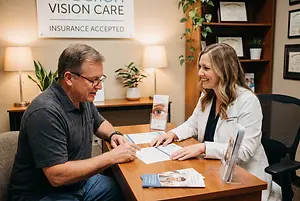 A man and a woman sit at a table in an office, looking at a document and smiling