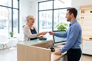 A man is handing a credit card to a woman behind a counter in an office building.