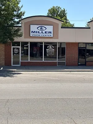 A Miller Vision Center building with a glass door and a glass wall with a reflection of a car and trees on a sunny day.