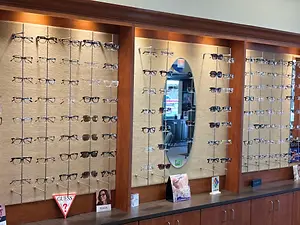 An array of eyeglasses and sunglasses displayed on a wall in an optic shop with wooden frames and a mirror.