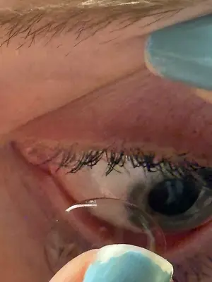 Close-up of an eye with a contact lens, eyelashes, and nail polish