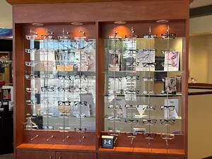 A display case with many glasses on a glass shelf with a reflection of the outside, a logo, and a book.