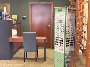 An interior view of an eyeglass store with a desk, chair, and wall-mounted glasses display