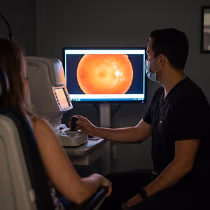 A woman sits in a chair while a man wearing a mask uses a medical device on her eye