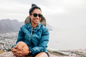 A woman sitting on a rock and smiling for a photo.