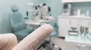 A finger holding a contact lens in front of a dental chair