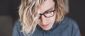 A closeup of a person wearing glasses, with their hair blowing in the wind, looking down.