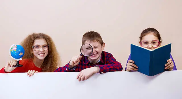 Three children sitting behind a banner holding a globe, a magnifying glass and a book