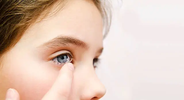 A girl wearing a contact lens while touching her eye.